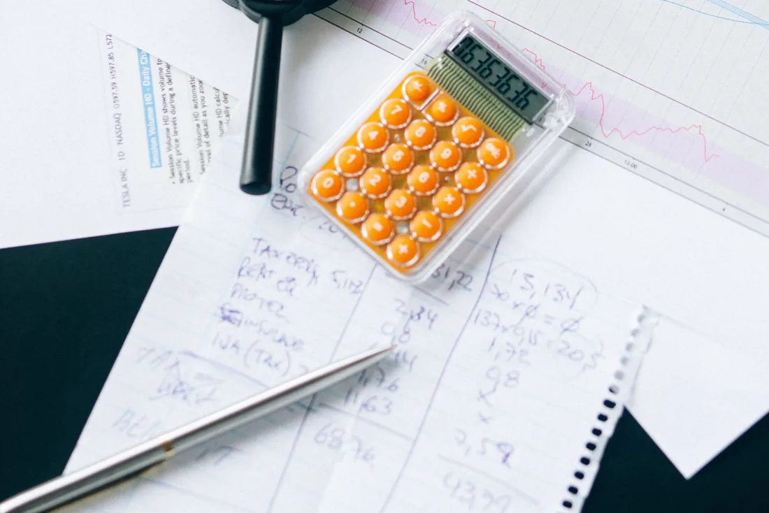 Calculatrice posée sur un relevé manuscrit de charges : loyer, assurance, TVA.